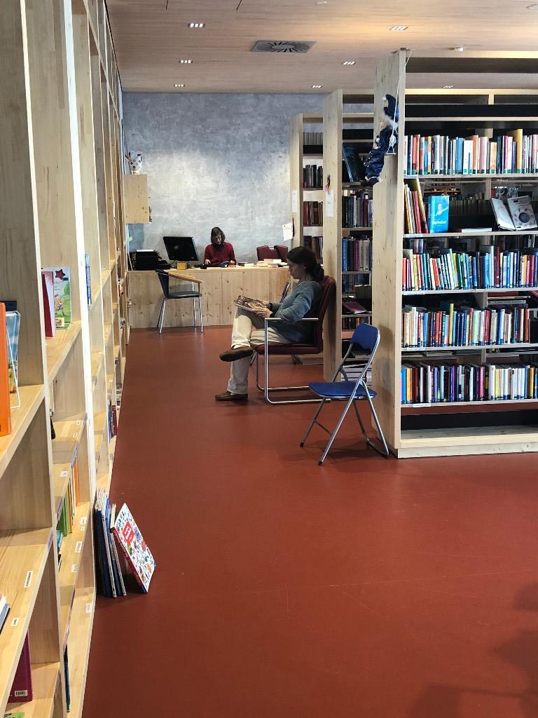 Links ein Regal rechts Regale im 90 Grad Winkel dazu. In der Mitte ein Gang