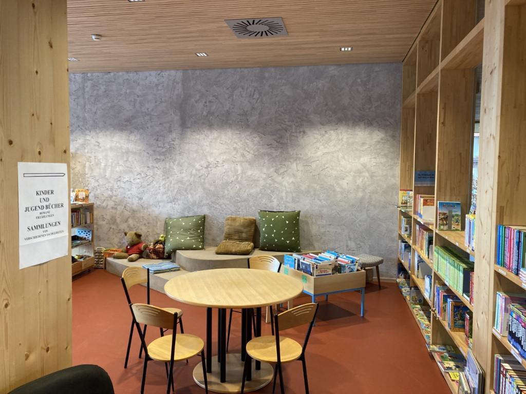 Tisch mit Stühlen und rechts im Bild Regale, hinten Couch und Kinderbereich